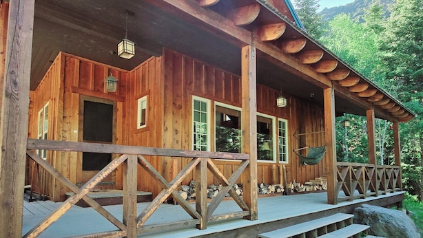 A wooden cabin with a porch, large windows, and a hanging chair.