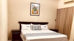 A hotel room with a bed, two bedside tables, a nightstand, a wall-mounted air conditioner, and a framed picture above the bed.