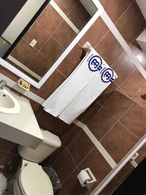 Een badkamer met bruine tegels, een witte wastafel, een toilet en een handdoek met een logo.