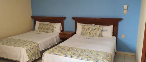 Two single beds with wooden headboards, white bedding, and patterned throw blankets in a room with blue walls and a tiled floor.