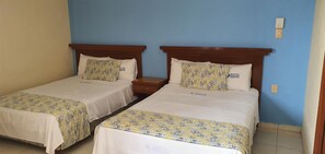 Twee enkele bedden met houten hoofdborden, witte beddengoed en beddengoed met een patroon in een kamer met blauwe wanden en een betegelde vloer.