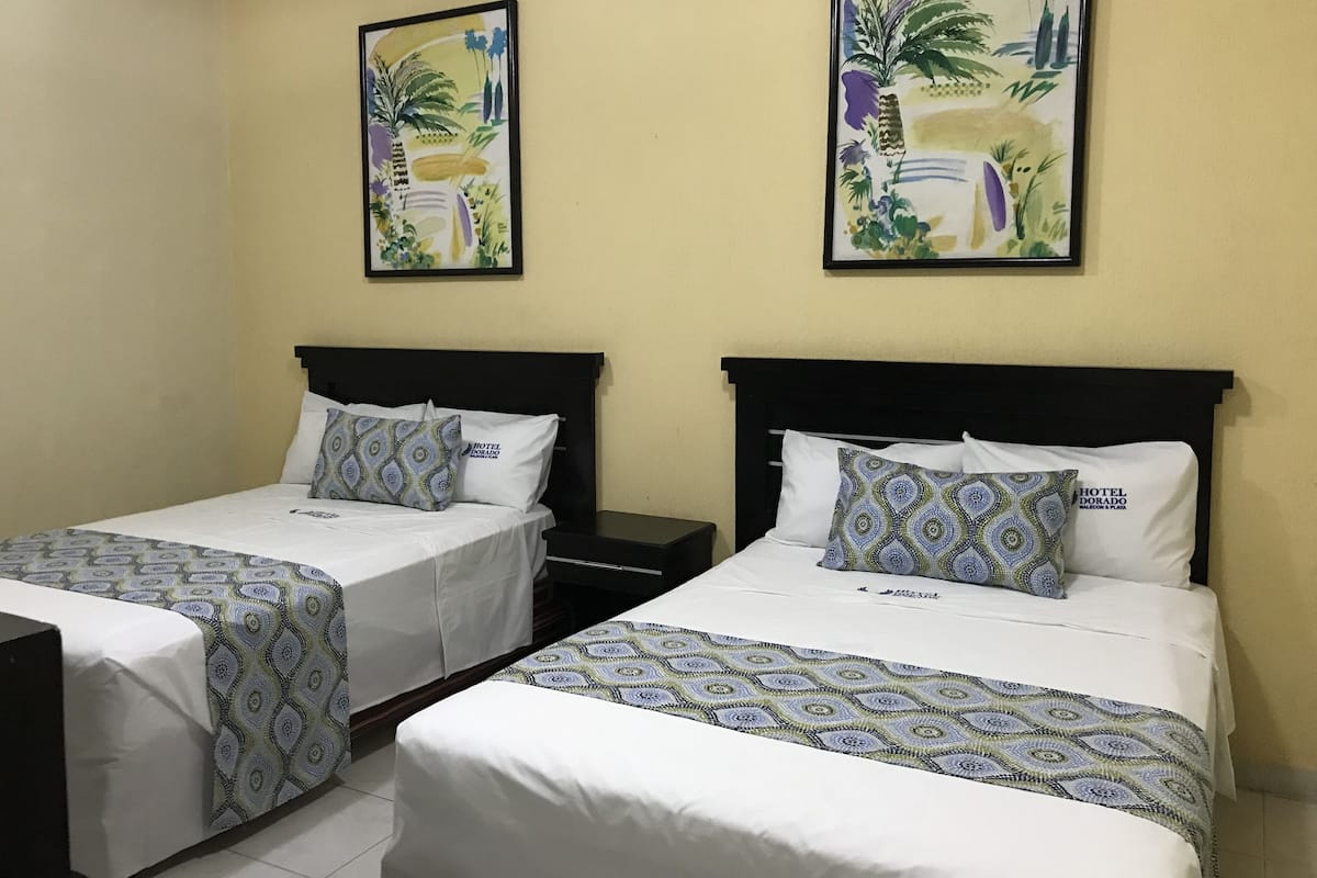 A hotel room with two beds, each with patterned bedding and pillows, and two framed floral paintings on the walls.