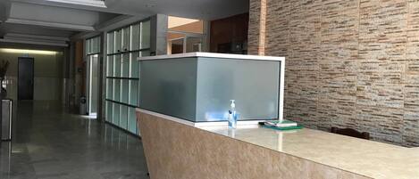 A reception area with a modern design, featuring a marble floor, a reception desk with a glass partition, and a textured wall.