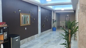 A hotel corridor with a dark wall, a framed mirror, a vending machine, and a potted plant.