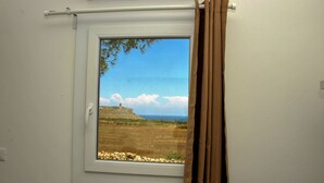 Una ventana con vista a un paisaje costero, que incluye un promontorio rocoso y el mar.