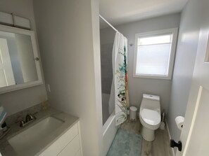 Et lille badeværelse med håndvask, toilet og bruseforhæng.