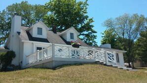 Ein zweistöckiges Haus mit weißer Fassade, einer Veranda mit Geländer und einem kleinen Garten mit Blumen.