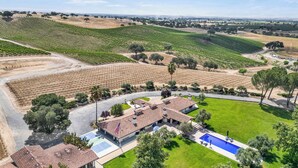 A vineyard with rows of grapevines, a swimming pool, and a building with a tiled roof. - Luxury Villa: Pool, Hot Tub, Pickleball, Ping-Pong & Bocce. 10 min to downtown! (Paso Robles)
