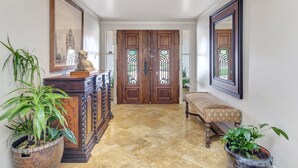 A hallway with a marble floor, a wooden bench, a large potted plant, a wooden cabinet, and a framed picture on the wall. - Luxury Villa: Pool, Hot Tub, Pickleball, Ping-Pong & Bocce. 10 min to downtown! (Paso Robles)