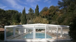 A covered swimming pool with a glass enclosure, surrounded by a stone patio. - Beautiful property located in a private domain with indoor and outdoor pool. (Draguignan)
