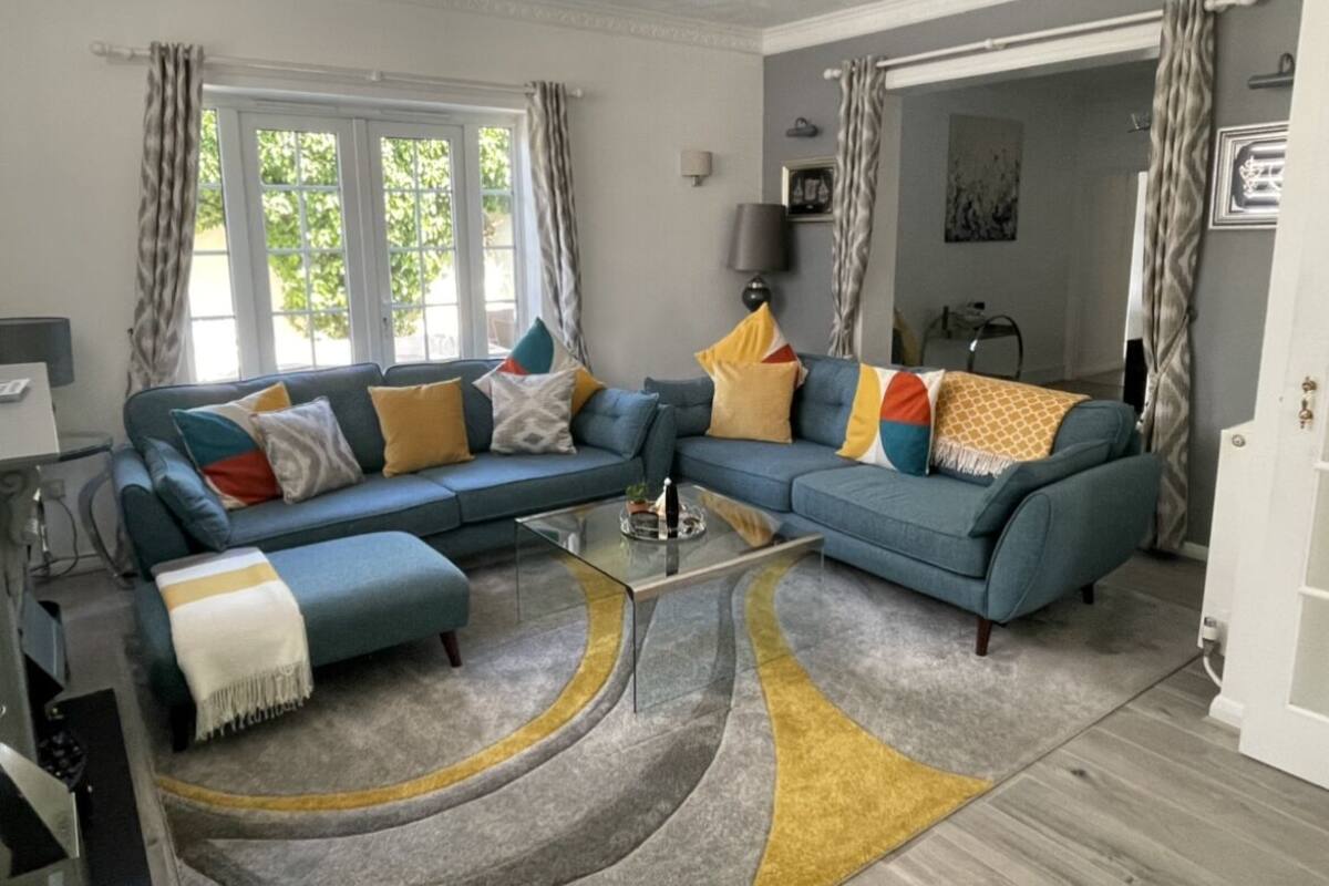 Un salon avec un canapé d’angle bleu, une table basse en verre et un tapis à motifs.