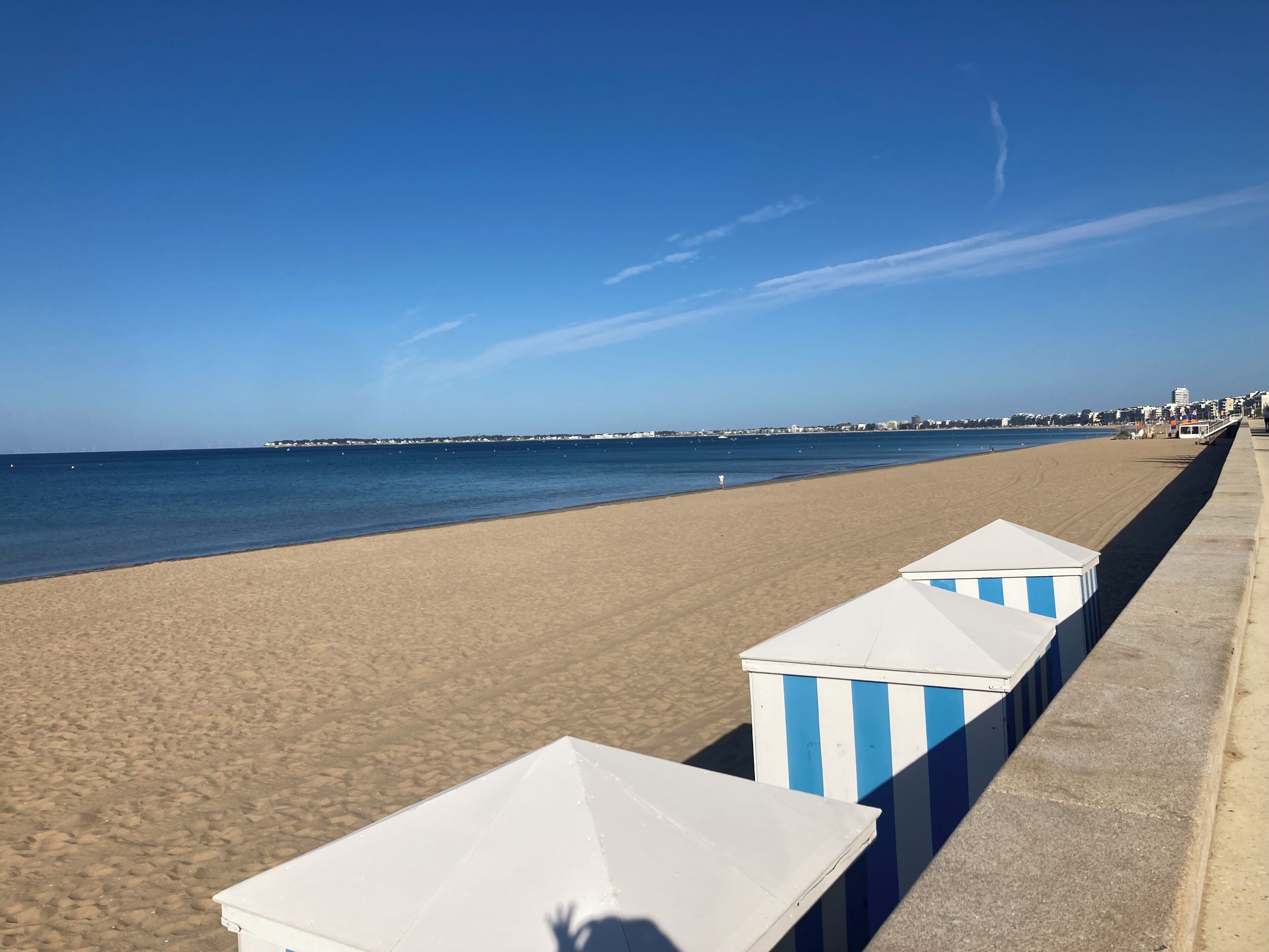A beach with a row of striped beach huts along the shore.