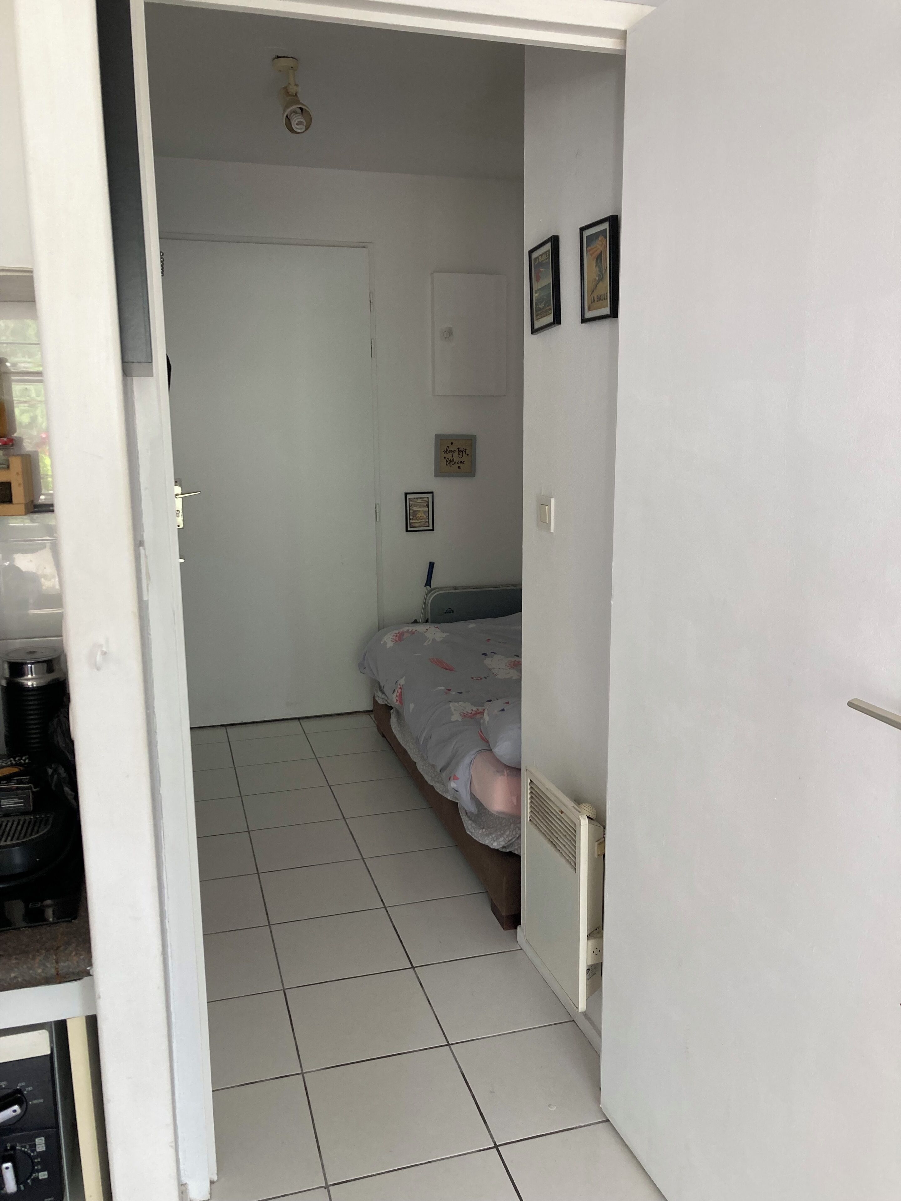 Ein Schlafzimmer mit einem Bett, einem Heizkörper, einer Tür und einem Fliesenboden.