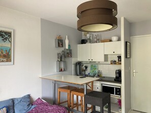 A compact kitchen with a dining area, a white door, and a wall-mounted shelf with various items.