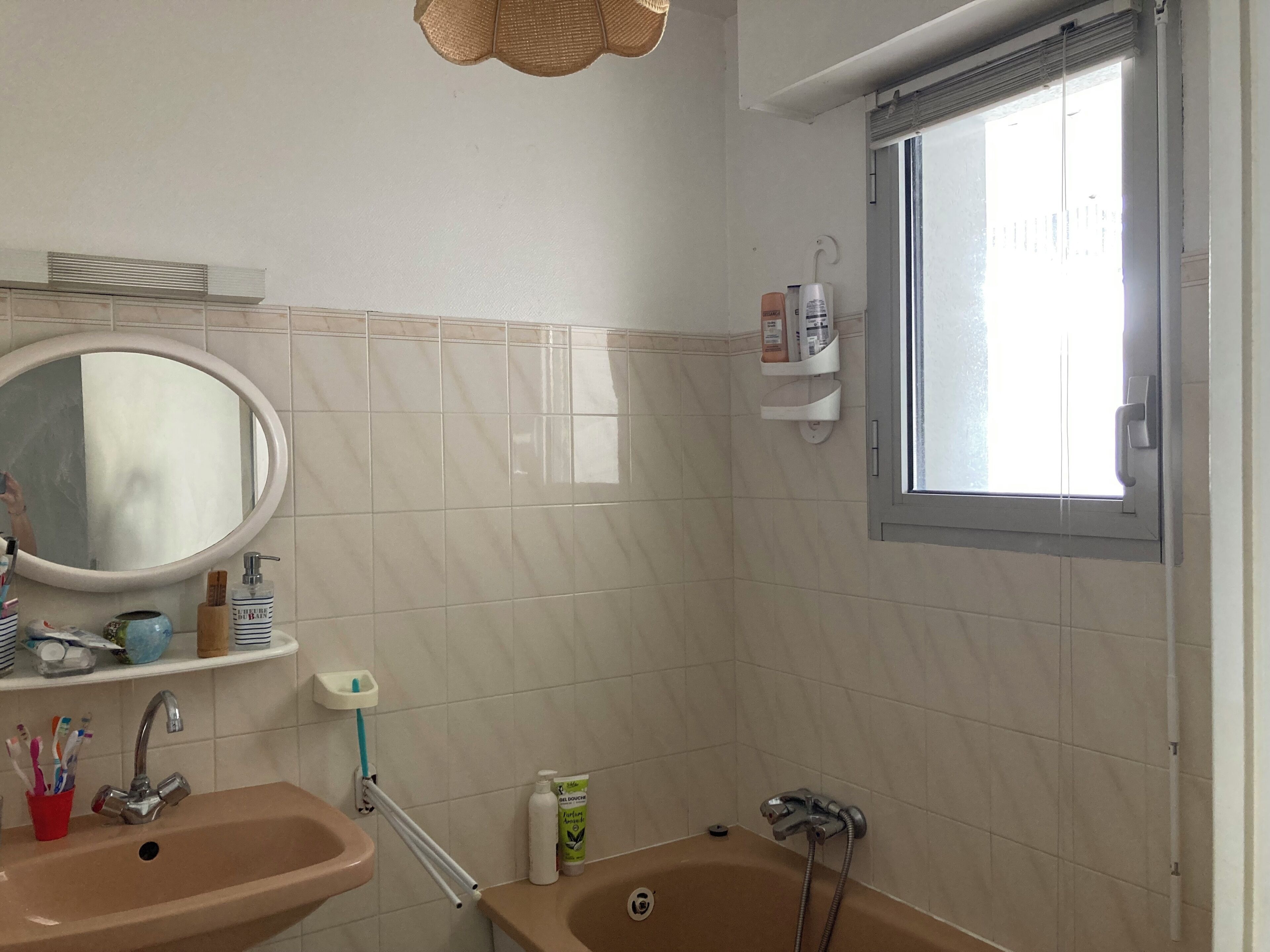 Baño con lavamanos, espejo, ventana y zona de ducha.