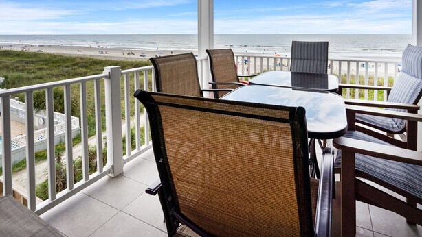 A balcony with wicker chairs and a table overlooking a beach. - Oceanfront views, amenities, all new luxury accommodations in popular Cherry Grove (North Myrtle Beach)