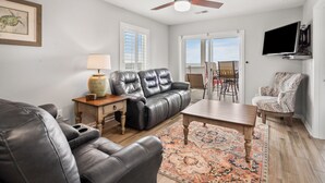 A living room with a sofa, a coffee table, a patterned rug, a television, and a ceiling fan. - Oceanfront views, amenities, all new luxury accommodations in popular Cherry Grove (North Myrtle Beach)
