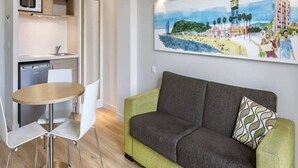 Un espace de vie compact comprenant un coin cuisine, un coin repas et un canapé, avec un tableau accroché au-dessus.