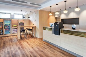 Un moderno vestíbulo de hotel con mostrador de recepción, zona de bar y máquinas expendedoras.