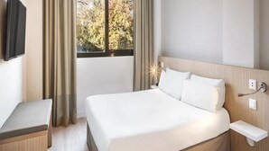 Une chambre d’hôtel avec un lit, une table de chevet et une fenêtre avec des rideaux.