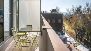 Un balcon extérieur avec une table et des chaises, donnant sur un jardin et un immeuble.