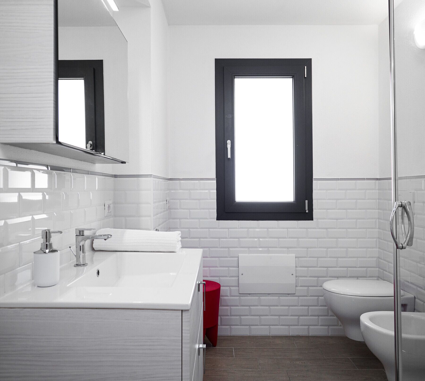 Un bany modern amb un lavabo blanc, un mirall, una finestra i un vàter.