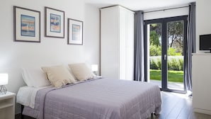 Un dormitorio con cama, mesita de noche, televisor y puerta corrediza de vidrio que da a un jardín.