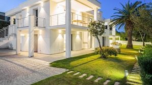Una casa moderna de dos pisos con un amplio jardín delantero, una escalera que lleva a la entrada y un balcón bien iluminado.