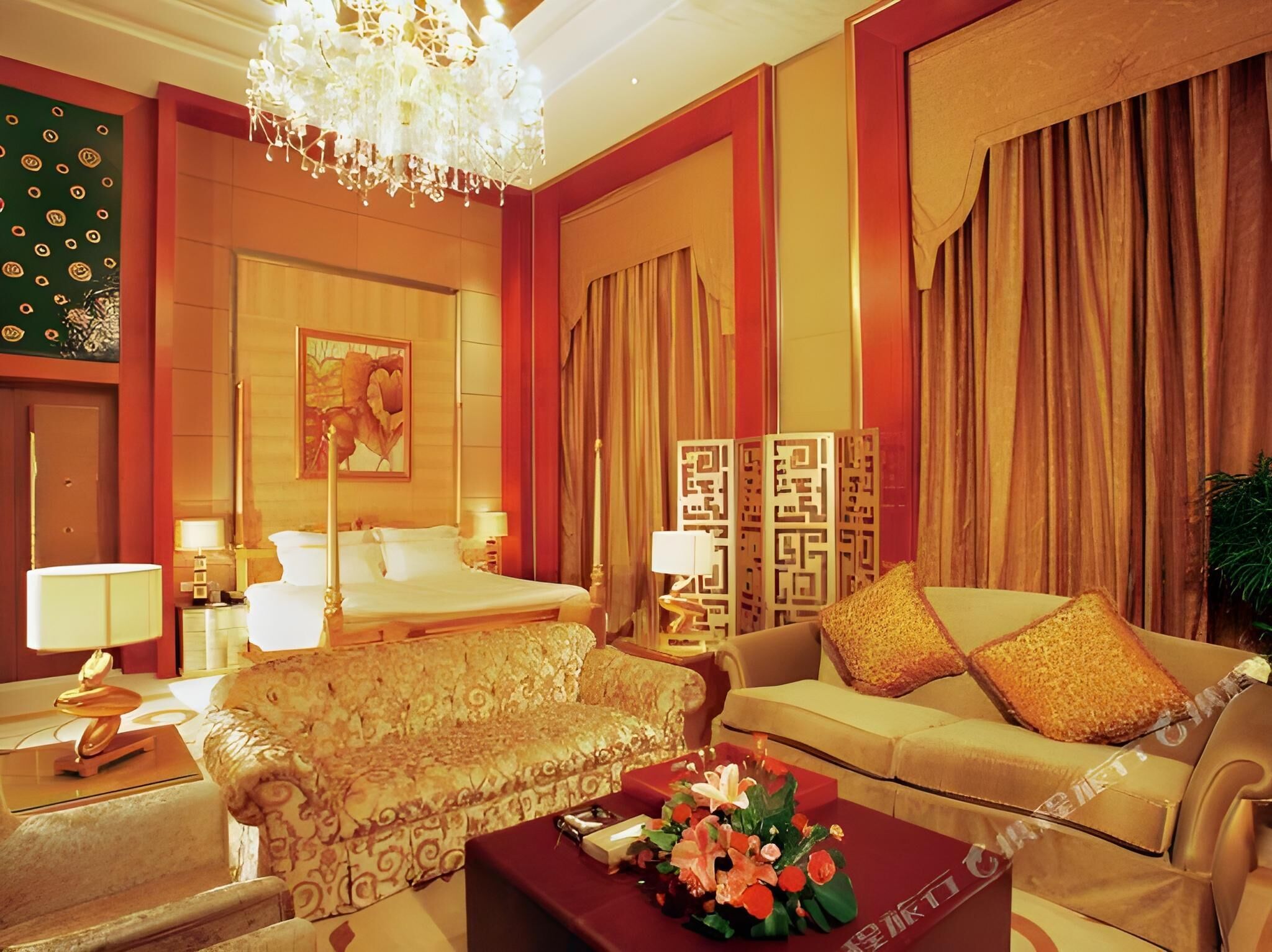 Habitación de hotel con cama, sofá, una mesa de centro con flores, un candelabro y un panel decorativo en la pared.