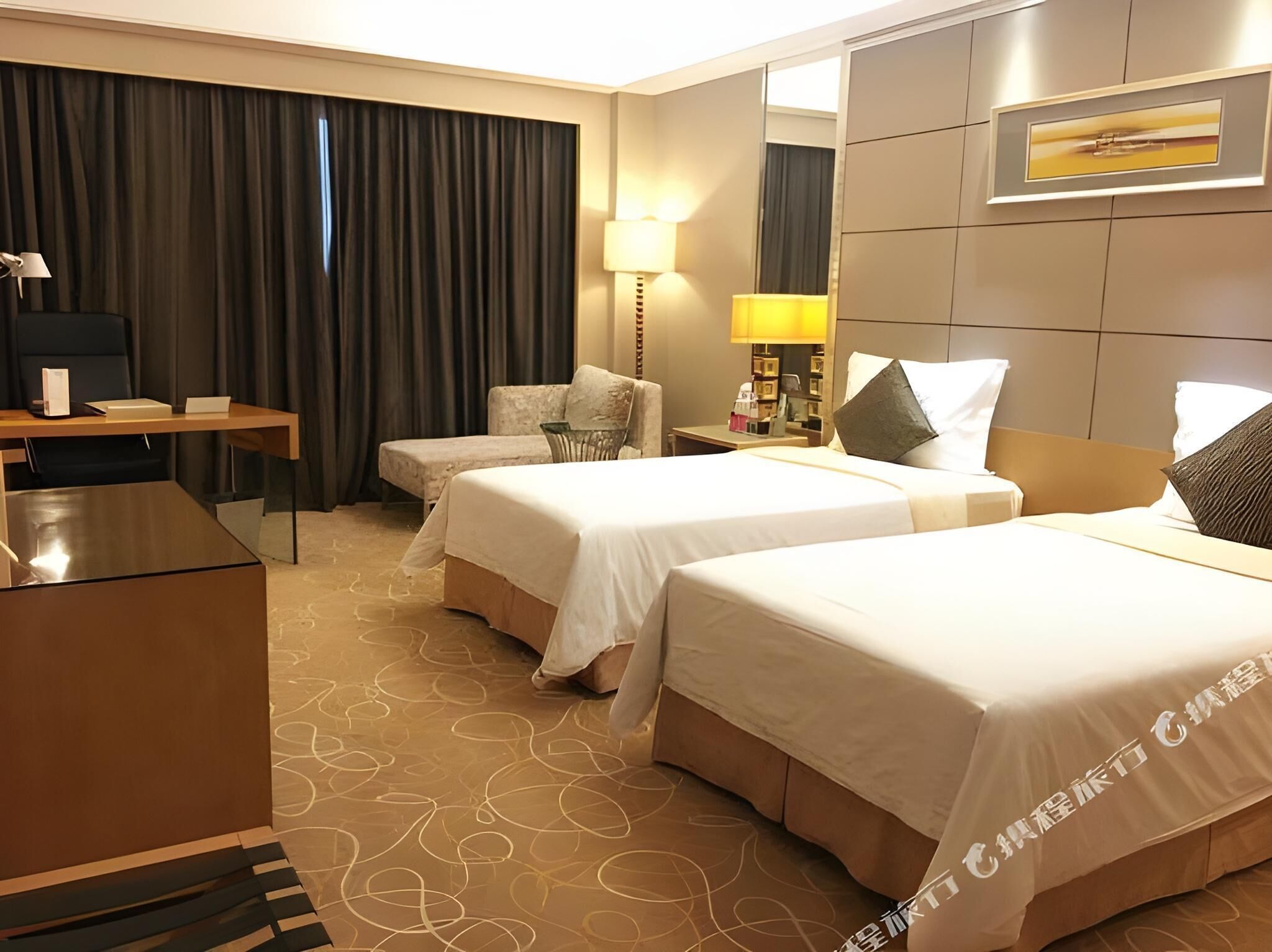 Ein Hotelzimmer mit zwei Betten, einem Schreibtisch, einem Stuhl, einer Lampe und einem großen Fenster mit Vorhängen.