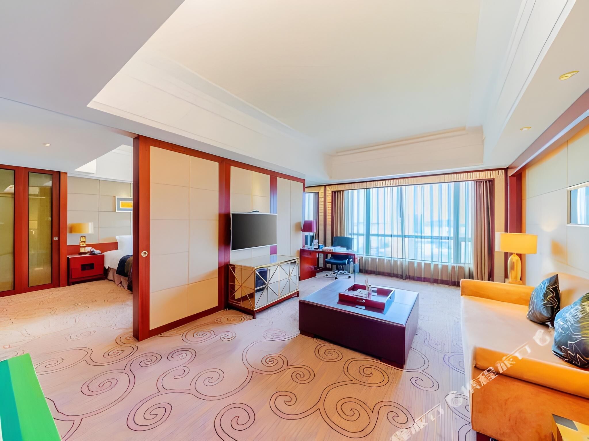 A hotel room with a bed, a TV, a desk, a sofa, and a large window with curtains.