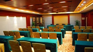 Un salón de conferencias con mesas y sillas dispuestas en filas, alfombra estampada y techo de madera con iluminación empotrada.