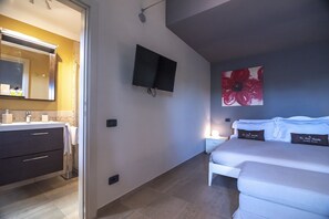 A modern hotel room with a bathroom, a flat-screen TV, a large floral artwork, and a bed with pillows. - Agriturismo Le Due Ruote (Grosseto)