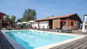 Una piscina con lettini e ombrelloni, circondata da un molo in legno e un edificio con tetto rosso.