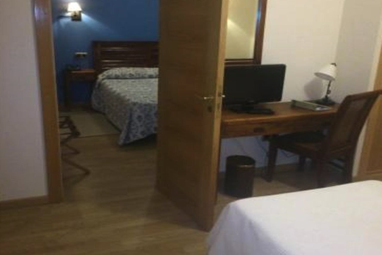 Una habitación de hotel con cama, escritorio, computadora, silla, lámpara y mesita de noche.