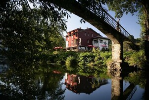Um edifício com fachada vermelha, uma ponte e um reflexo na água.