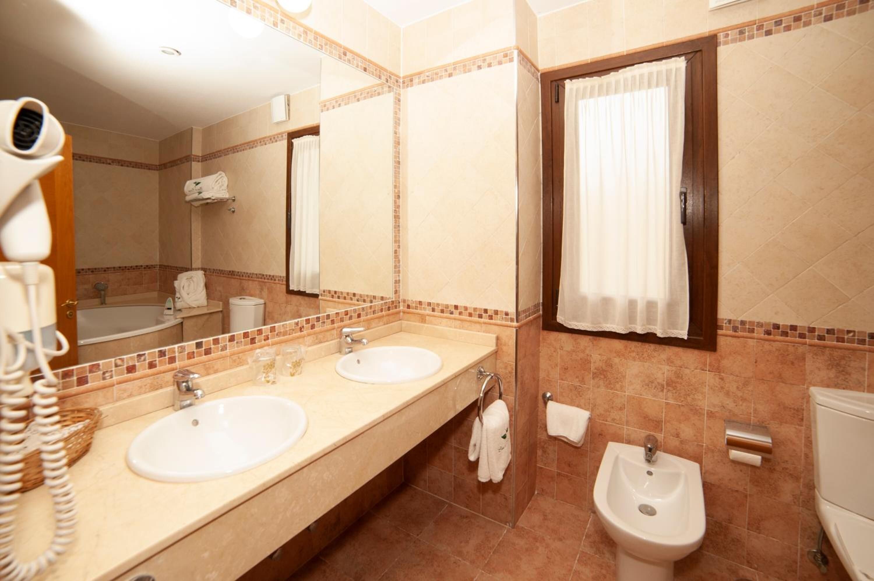 Un bany d'hotel amb dues dutxes, un vàter, una barra de tovalloles i un assecador.