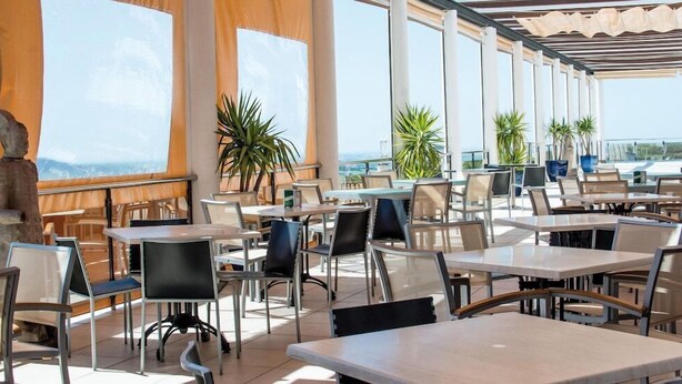 An outdoor cafe with tables and chairs, large windows, and potted plants. - Hotel ATH Al Medina Wellness (Medina-Sidonia)