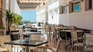 An outdoor cafe with tables and chairs, a tiled floor, and a view of the sea. - Hotel ATH Al Medina Wellness (Medina-Sidonia)