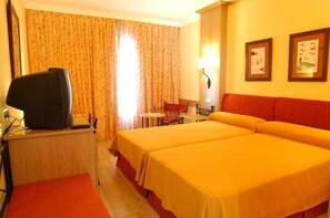 Habitación de hotel con dos camas, un escritorio con televisor, una silla y una lámpara.