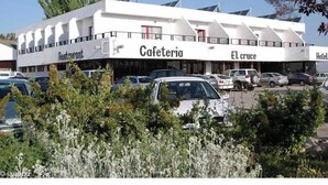 A building with a 'Cafeteria' sign, 'El cruce' and 'Hotel' signs, and a parking lot with cars. - El Cruce (Manzanares)