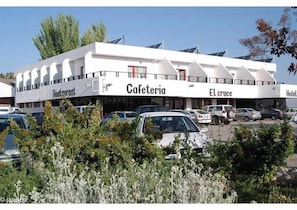 A building with a 'Cafeteria' sign, 'El cruce' and 'Hotel' signs, and a parking lot with cars. - El Cruce (Manzanares)