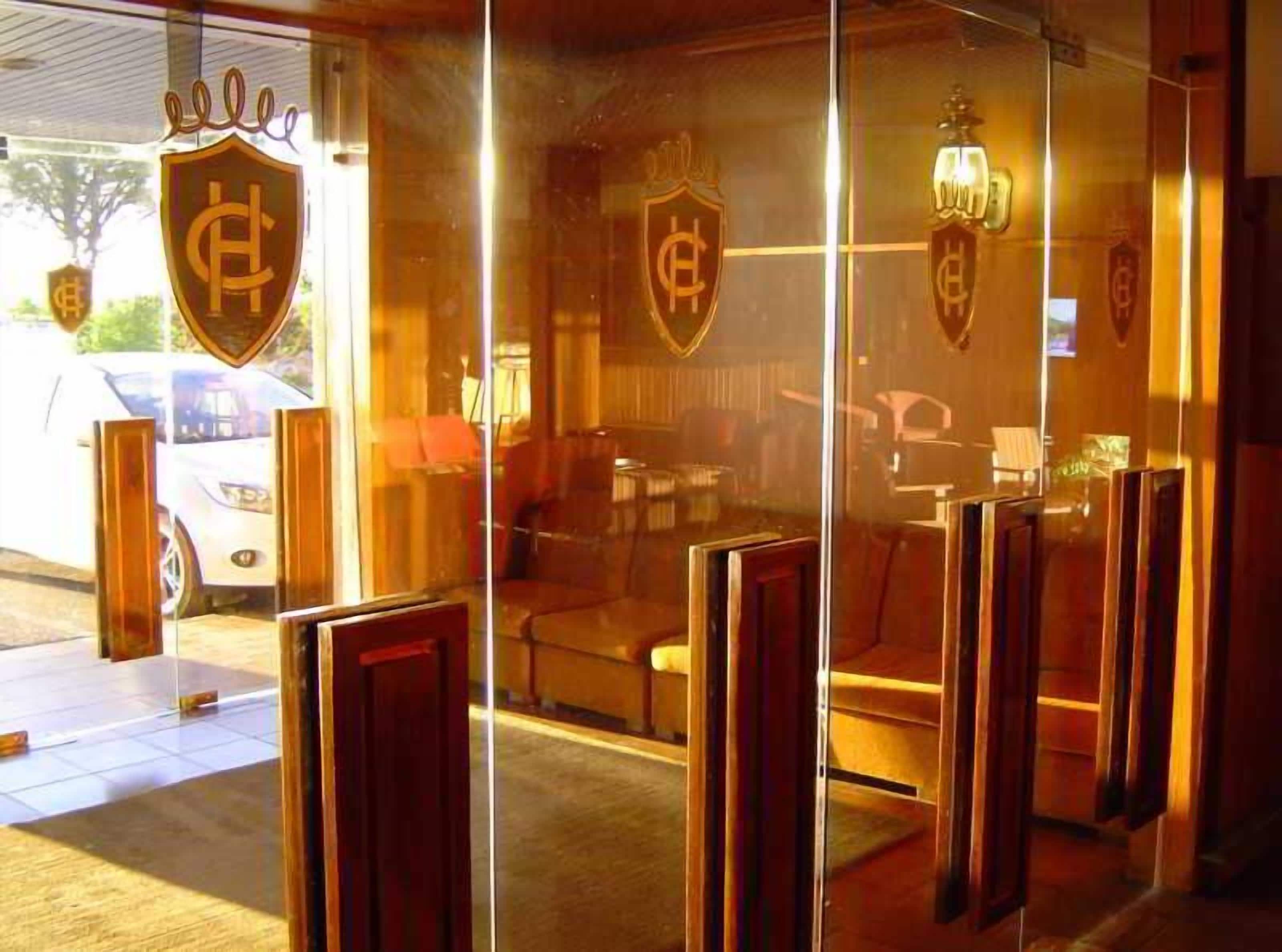 Entrada de un hotel con puertas de cristal, un mostrador de recepción y un coche estacionado afuera.