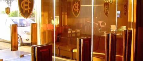 Entrada de un hotel con puertas de cristal, un mostrador de recepción y un coche estacionado afuera.