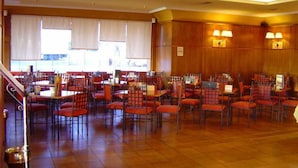 Un comedor amplio con varias mesas y sillas, una escalera y ventanas grandes.