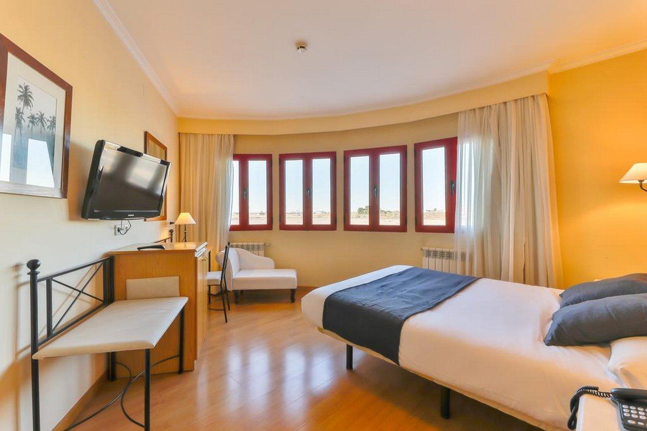 A hotel room with a bed, a desk, a chair, a television, and a window with curtains.