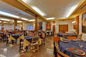 Comedor de hotel con varias mesas y sillas, dispuesto en un espacio amplio.