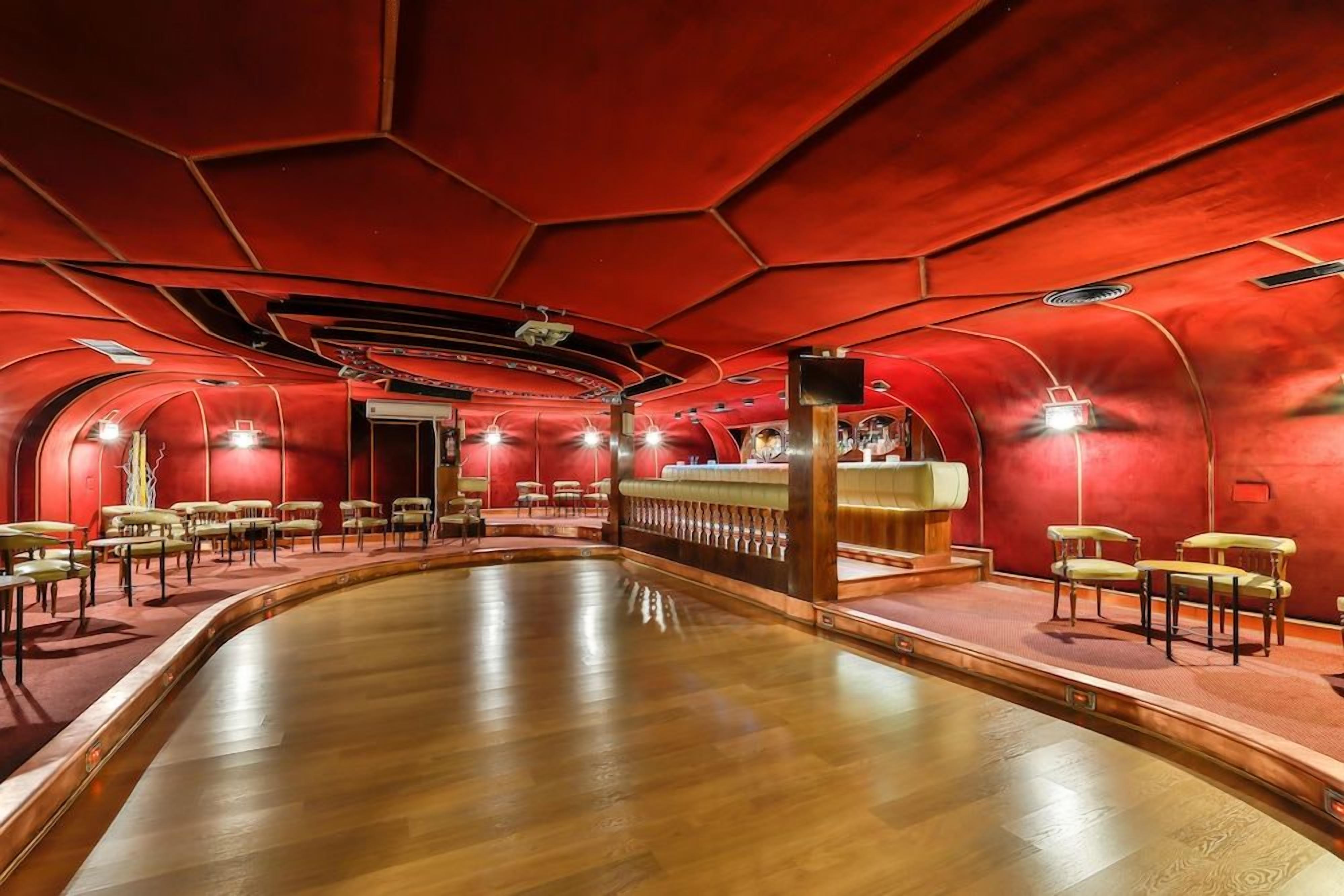 Una habitación con piso de madera curvada, paredes rojas y una zona de bar con taburetes.