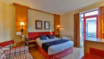 A hotel room with a bed, two bedside tables, a chair, a desk, and a window with curtains.