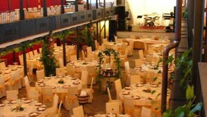 A banquet hall with round tables set for dining, a stage with musical instruments, and a staircase leading to an upper level. - El Cruce (Manzanares)